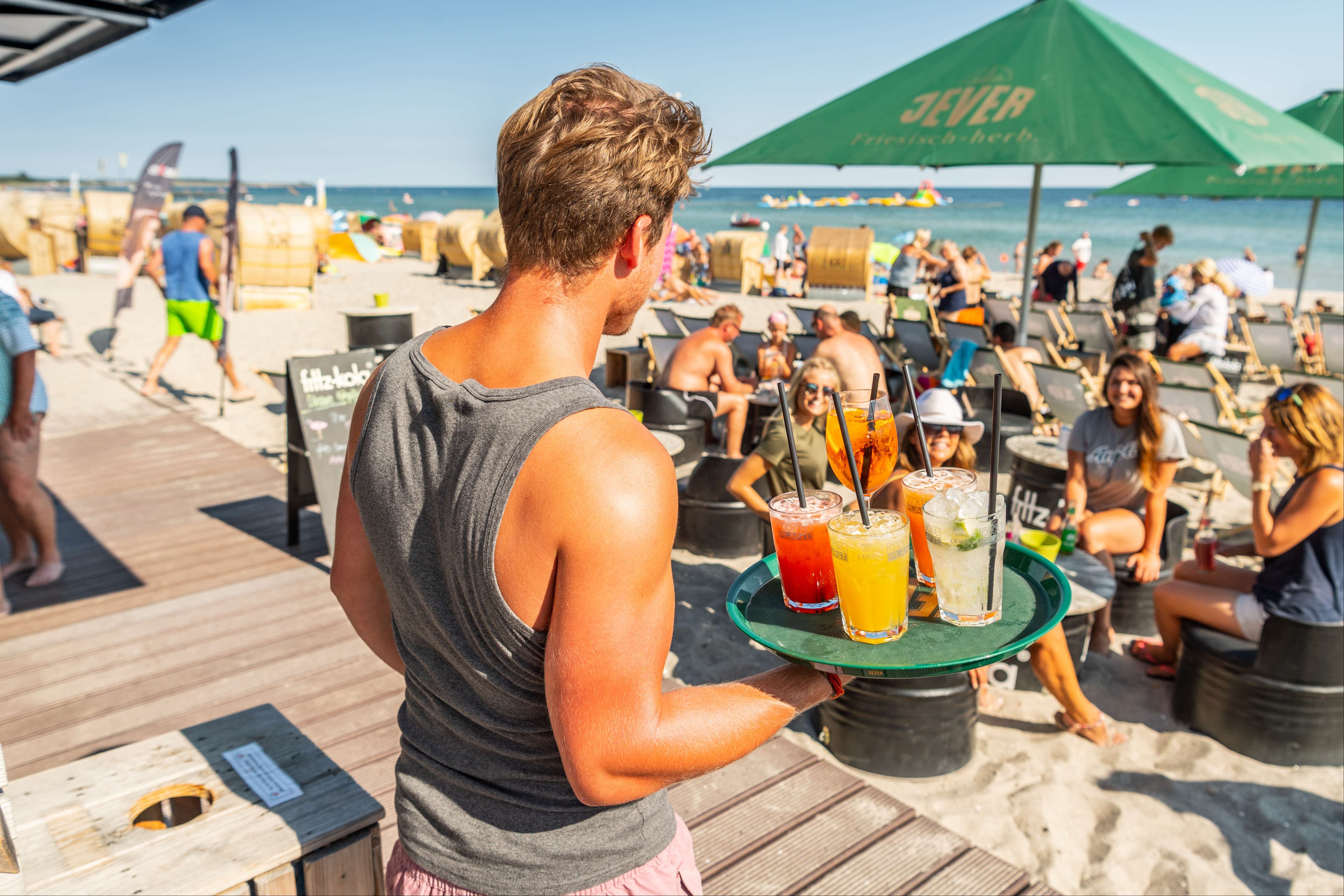 Kellner serviert Cocktails an einer Strandbar bei Sonnenschein und warmen Temperaturen.