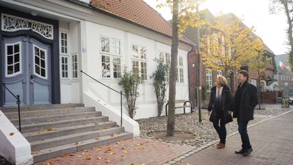 Ein Paar geht im Herbst in Burg, vorbei am Senator-Thomsen-Haus spazieren