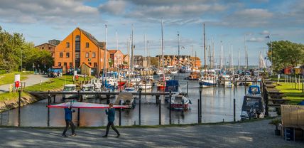 Zwei Personen tragen ein Windsurfsegel im Orther Hafen