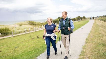 Ein Paar Wandert mit Nordic Walking Stöcken auf dem Deich in Altenteil