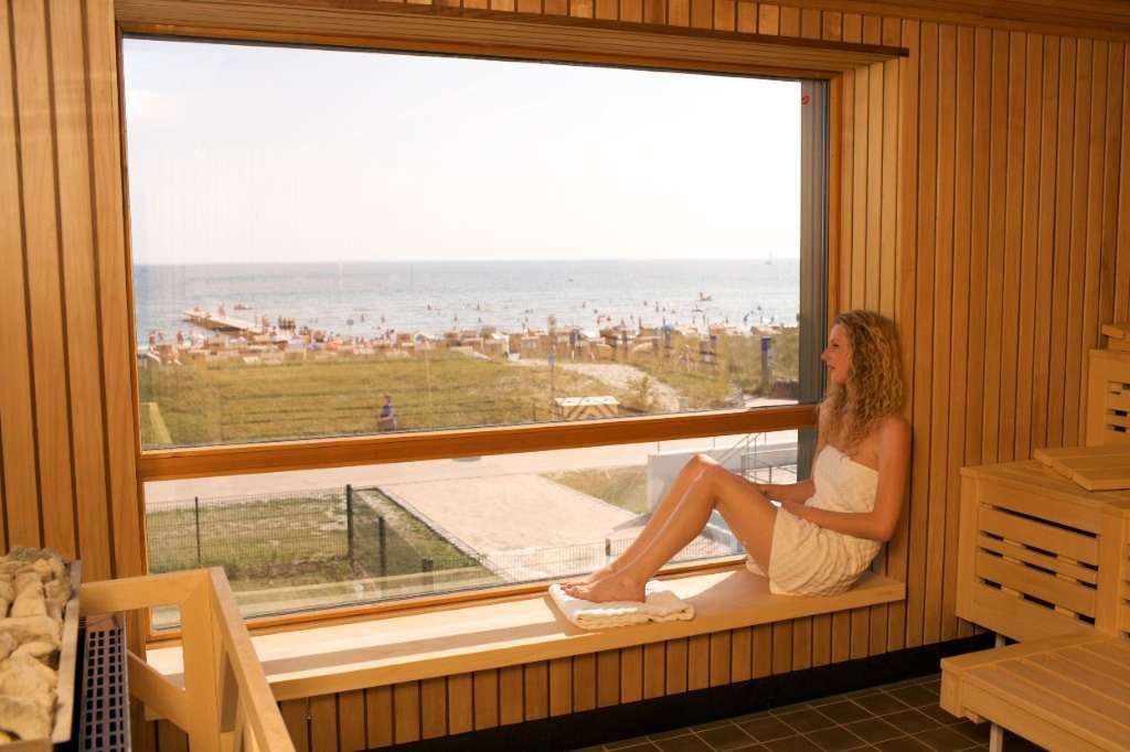 Eine Frau sitzt in der Panoramasauna in der FehMare Wellnesswelt und schaut auf die Ostsee