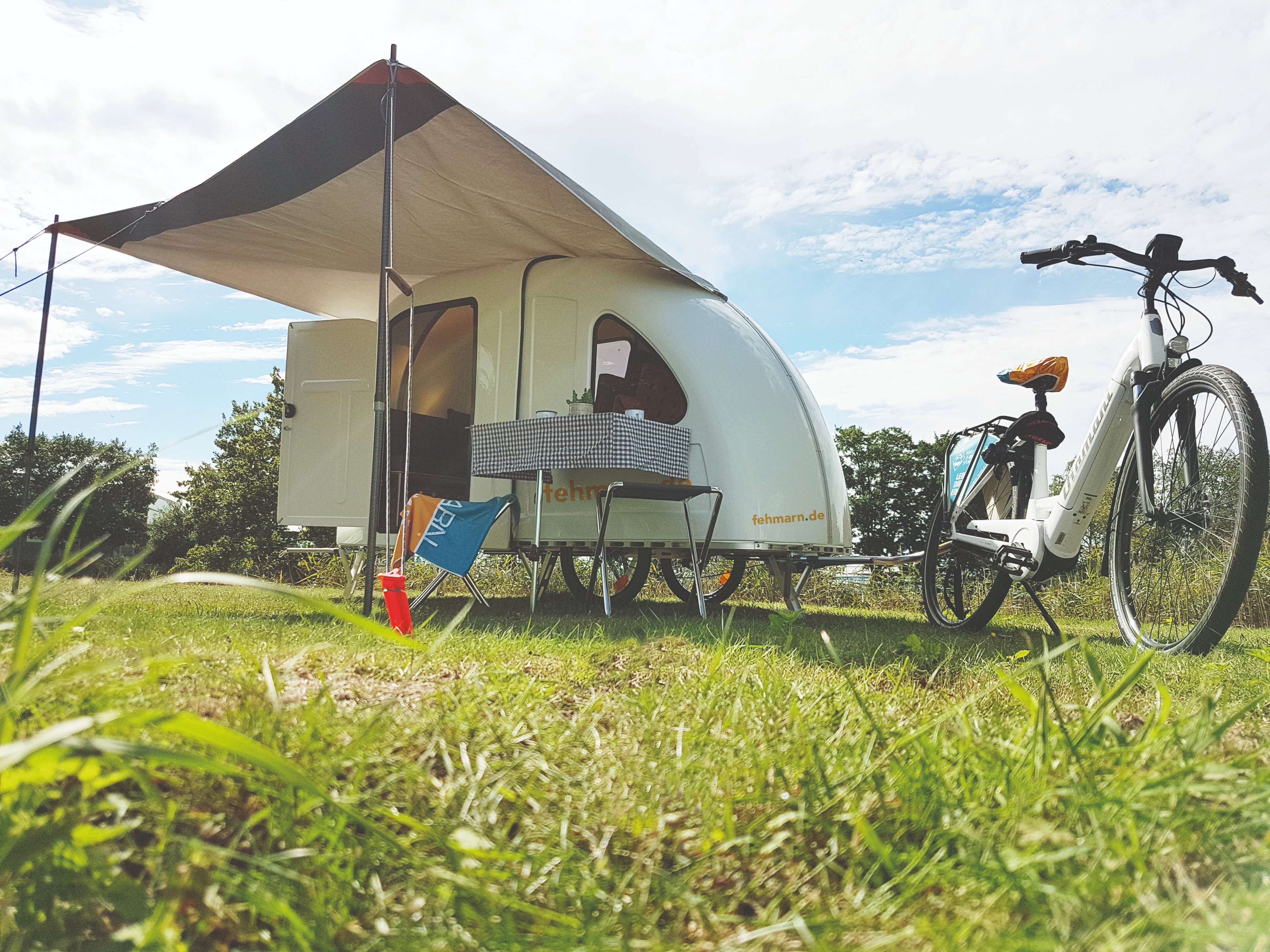 Ein Mini-Wohnwagen, der ausgeklappt auf einer Wiese steht mit einem E-Bike.