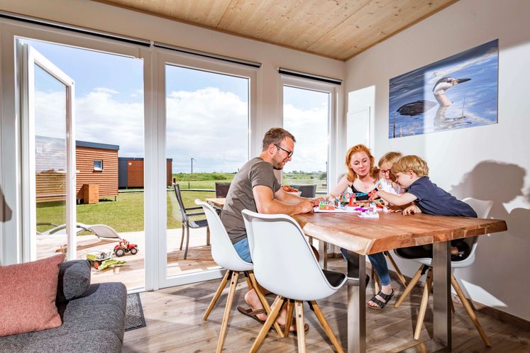 Junge Familie sitzt am Esstisch in einem modernen Tinyhouse auf einem Campingplatz