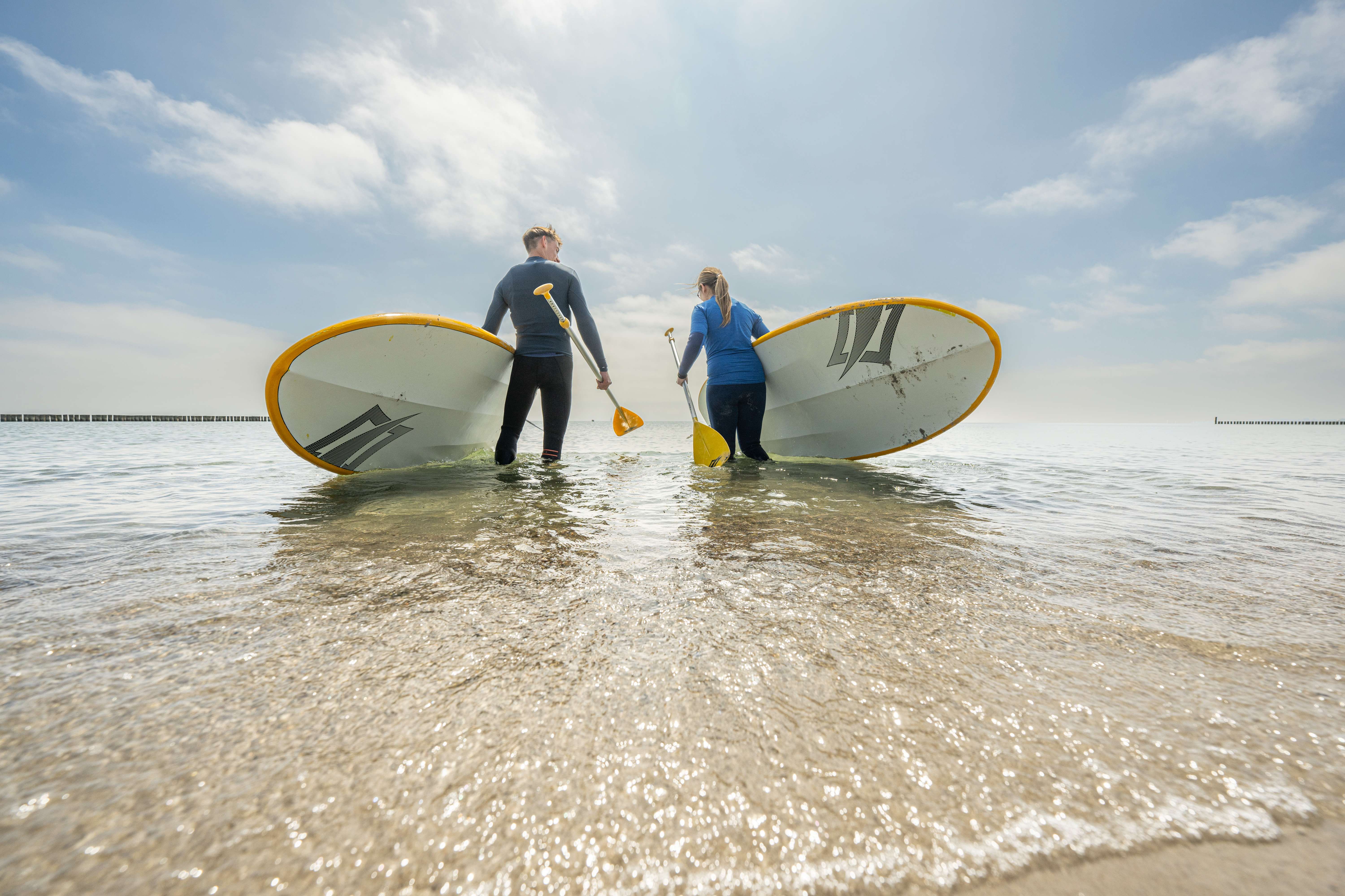 Zwei Personen tragen Stand Up Paddle Boards in die Ostsee 